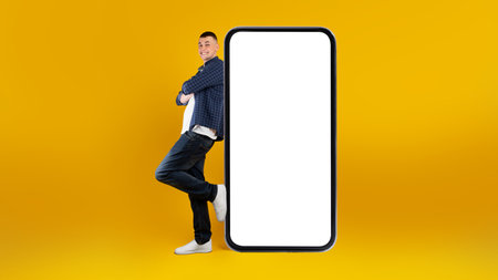Young Smiling Man Leaning Against a Large Blank Smartphone on a Bright Yellow Background