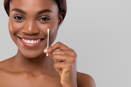Smiling Woman Holding Cotton Swab While Applying Skincare in Bright Atmosphereの写真素材