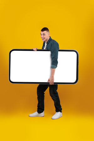 Young Man Holds Large Empty Sign Against Vibrant Yellow Background During Creative Photoshoot