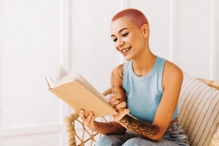 Woman Enjoying Reading a Book While Sitting in a Cozy Setting With a Smileの写真素材
