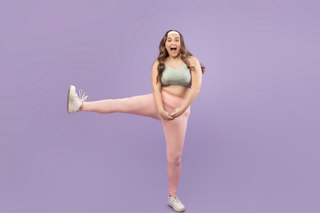 Joyful Young European Plus Size Female Athlete Jumps With Excitement on Purple Backgroundの写真素材