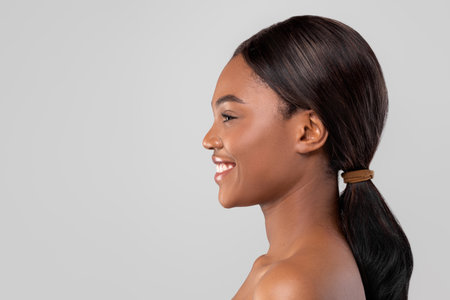 Young Woman Smiling With Long Hair Tied Back, Showcasing Her Profile Against a Gray Backgroundの写真素材