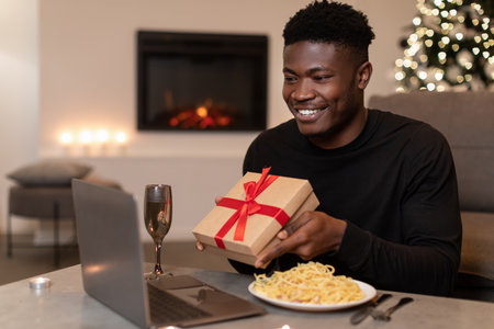 Black Man Celebrating Holidays With Video Call While Showing Gift Box at Home Dinner