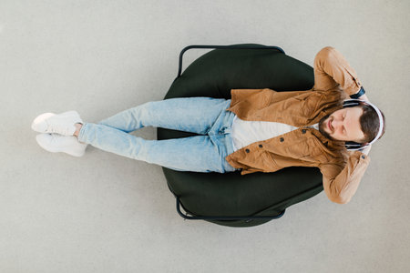 Man Relaxing in a Chair With Headphones On, Enjoying Music in a Modern Indoor Space During Daytimeの写真素材