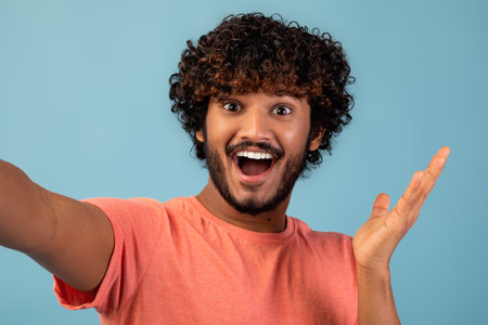 Emotional Young Hindu Man Happily Taking Selfie Against a Blue Background