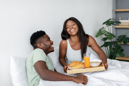 Couple Enjoys Breakfast in Bed With Smiles, Sharing Quality Time Together in a Cozy Roomの写真素材