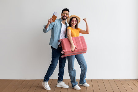 Happy Couple Excited for Their Vacation Holding Tickets and a Suitcase in a Bright Indoor Areaの写真素材
