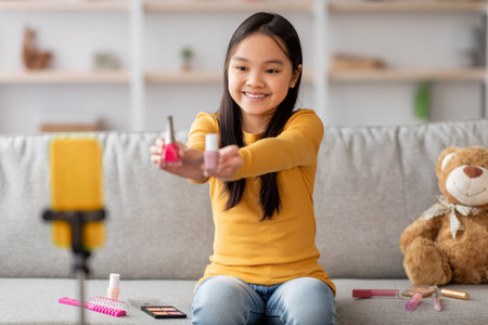 Girl Shows Nail Polish and Beauty Products While Recording a Video in a Cozy Living Room Settingの写真素材
