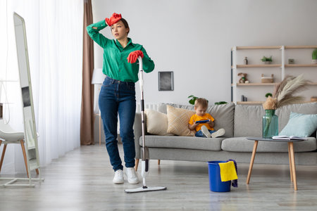 Woman Cleaning Living Room While Child Plays Nearby in Modern Home Settingの写真素材