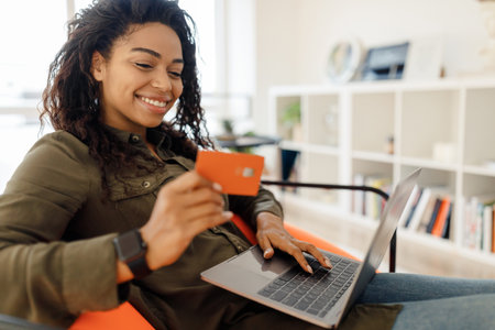 Young Woman Shopping Online With a Credit Card and Laptop in a Cozy Living Room Settingの写真素材