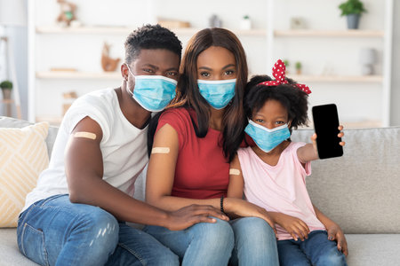 Family Smiles While Showing Their Vaccination Status at Home in a Cozy Living Room Settingの写真素材
