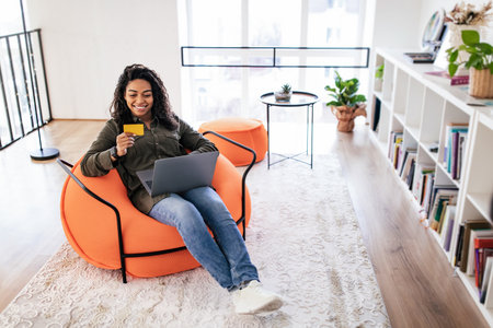 Woman Enjoys Online Shopping While Sitting on a Comfortable Chair in a Modern Living Roomの写真素材