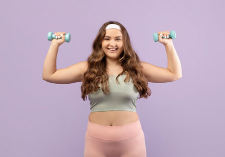 Pretty Young Plus Size Female Exercising With Dumbbells Against a Purple Background