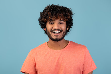 Positive Handsome Young Man With Curly Hair and Beard on Blue Background in a Pink Shirt