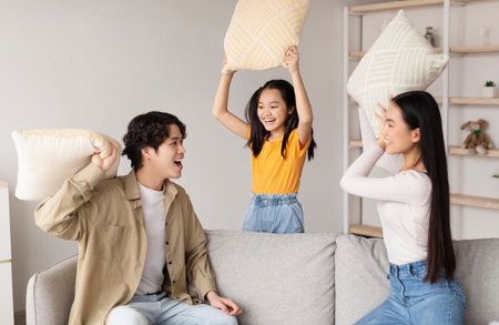 Family Enjoys a Playful Pillow Fight in a Cozy Living Room Setting During the Afternoonの写真素材