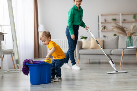 Child Helping With Cleaning While Adult Vacuums Living Room During Daytimeの写真素材