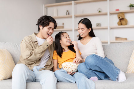 Family Enjoying Snack Time Together on the Couch in a Cozy Living Roomの写真素材
