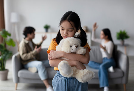 Child Holding Teddy Bear While Parents Argue in the Background at Homeの写真素材