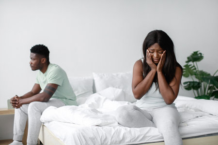 Tension Fills the Air as a Couple Sits Apart on Their Bed During a Moment of Conflict in a Bright, Modern Roomの写真素材