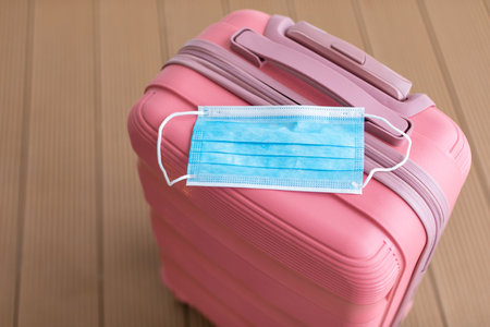 Pink Suitcase With a Blue Face Mask Resting on Top, Ready for Travel in a Safe Environmentの写真素材