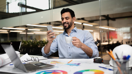 Man Enjoying Coffee While Checking Phone in Modern Office Space During Work Hoursの写真素材