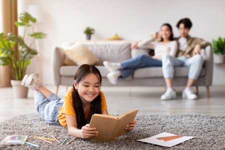 Child Enjoys Reading on the Floor While Parents Relax on the Couch in a Cozy Living Room Settingの写真素材