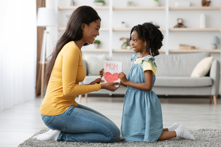 Mother and Daughter Sharing a Heartfelt Moment With a Handmade Card in a Cozy Living Roomの写真素材