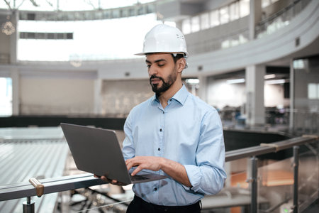 Engineer Working on Laptop in Modern Industrial Space During Daylight Hours