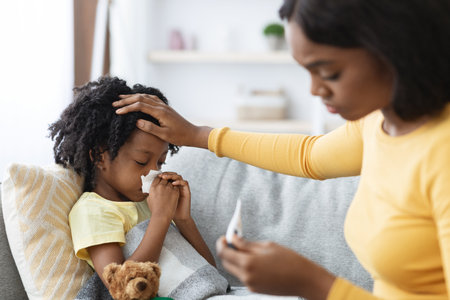 Caring Mother Comforts Her Sick Child While Checking Temperature on the Couch at Homeの写真素材