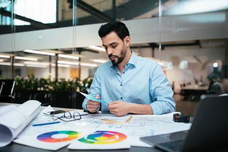 Professional Man Analyzing Design Plans and Color Palettes in a Modern Office Environment During Daylight Hoursの写真素材