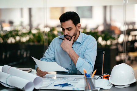 Engineer Reviewing Architectural Plans in Modern Office Space During Working Hoursの写真素材