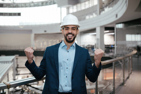 Professional Man Celebrating Success in Modern Office Space With a Hard Hat While Wearing a Suitの写真素材