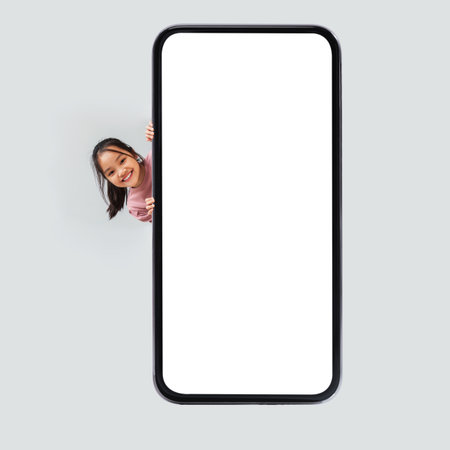 Japanese Girl Happily Posing Near a Large Blank Phone Screen in a Studio Settingの写真素材