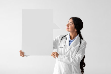 Young Woman Doctor in White Coat Holds Empty Space for Health Advice on Light Backgroundの写真素材