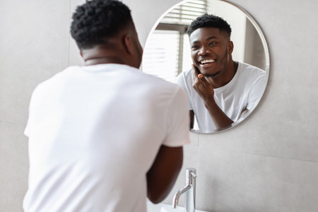 Black Man Smiling at Reflection While Preparing for Grooming in Modern Bathroomの写真素材