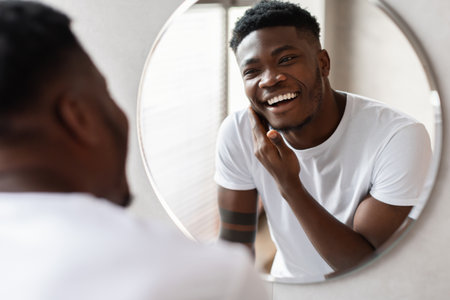 Unshaven Man Smiles at Reflection While Preparing for Shaving in Modern Bathroomの写真素材