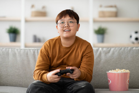 Happy Asian Boy Enjoys Gaming and Popcorn at Home During Weekend With Family