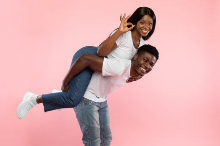Joyful Black Couple Sharing Fun Moments With Playful Gestures in a Pink Studio Settingの写真素材