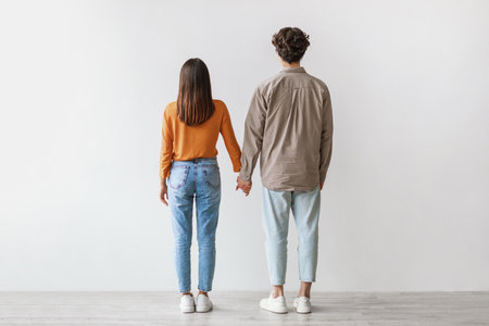 Young Asian Couple Holds Hands in Casual Attire Against White Studio Wallの写真素材