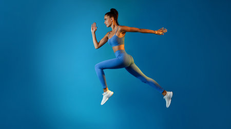 Young Sportswoman Jumps With Determination in Mid-Air on a Blue Studio Backgroundの写真素材