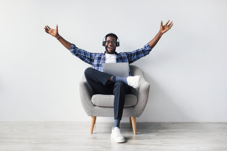 Excited Young Man in Headphones Engaging in Online Conversation While Sitting in Chairの写真素材