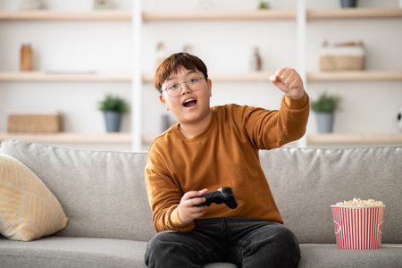 Emotional Asian Boy Enjoying Video Games and Popcorn in Cozy Living Room on Weekendの写真素材