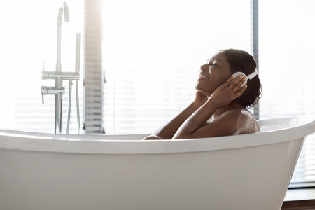 Relaxing Bath Time for Young Woman Enjoying Music in Bright Bathroomの写真素材
