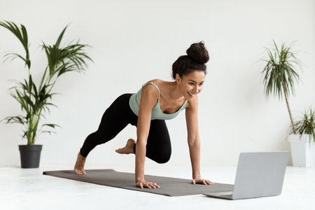 Sporty Woman Engaged in Fitness Training at Home Watching Online Tutorials on a Laptopの写真素材