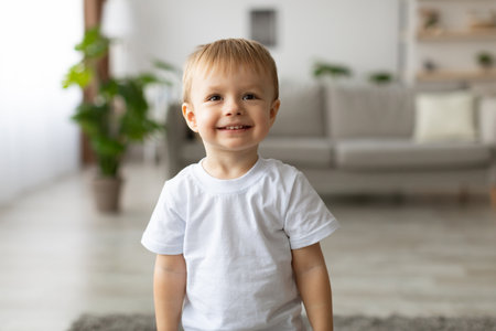 Smiling Young Boy in a Bright Living Room Wearing a White T-Shirt Enjoying a Moment of Happiness Indoorsの写真素材