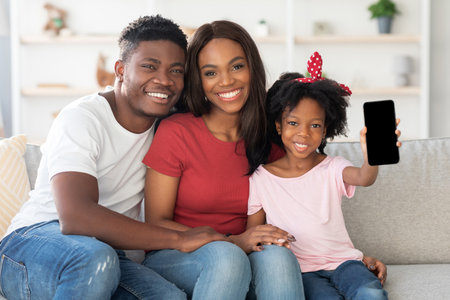 Joyful Family Poses Together on a Cozy Sofa While the Daughter Shows off Her Smartphone in a Living...