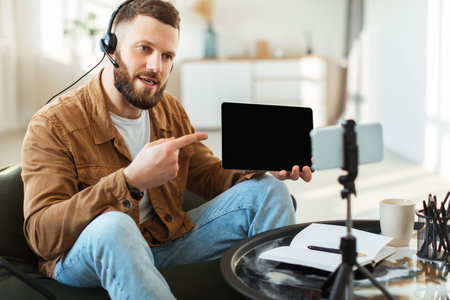 Man Using Tablet and Smartphone to Communicate During Online Meeting at Home Workspace in Daytimeの写真素材
