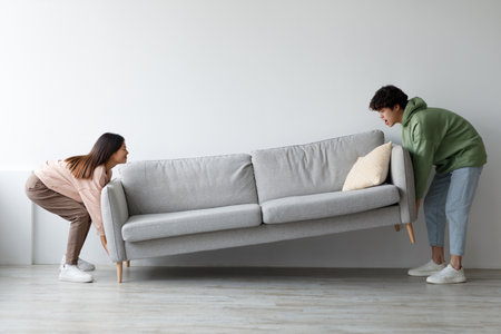 Young Couple Happily Moving Sofa Together to Refresh Living Room Space at Homeの写真素材