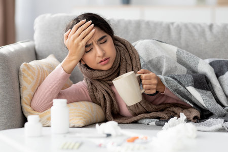 Young Woman in Plaid Blanket Looks Unwell While Drinking Tea at Home During Illness