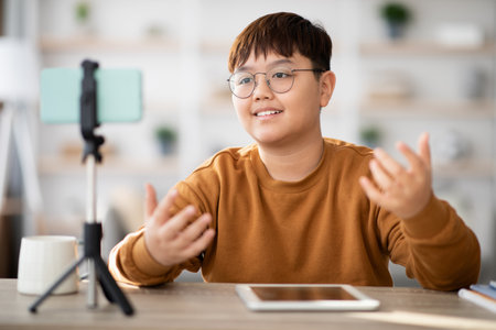 Cheerful Teenager Streaming a Vlog From Home Using a Cellphone and Digital Tabletの写真素材